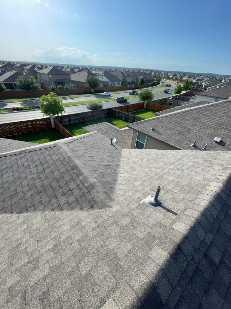 The view from on top of a gray shingle roof in a neighborhood near San Antonio, Texas, with a pipe boot and several roof planes in the foreground