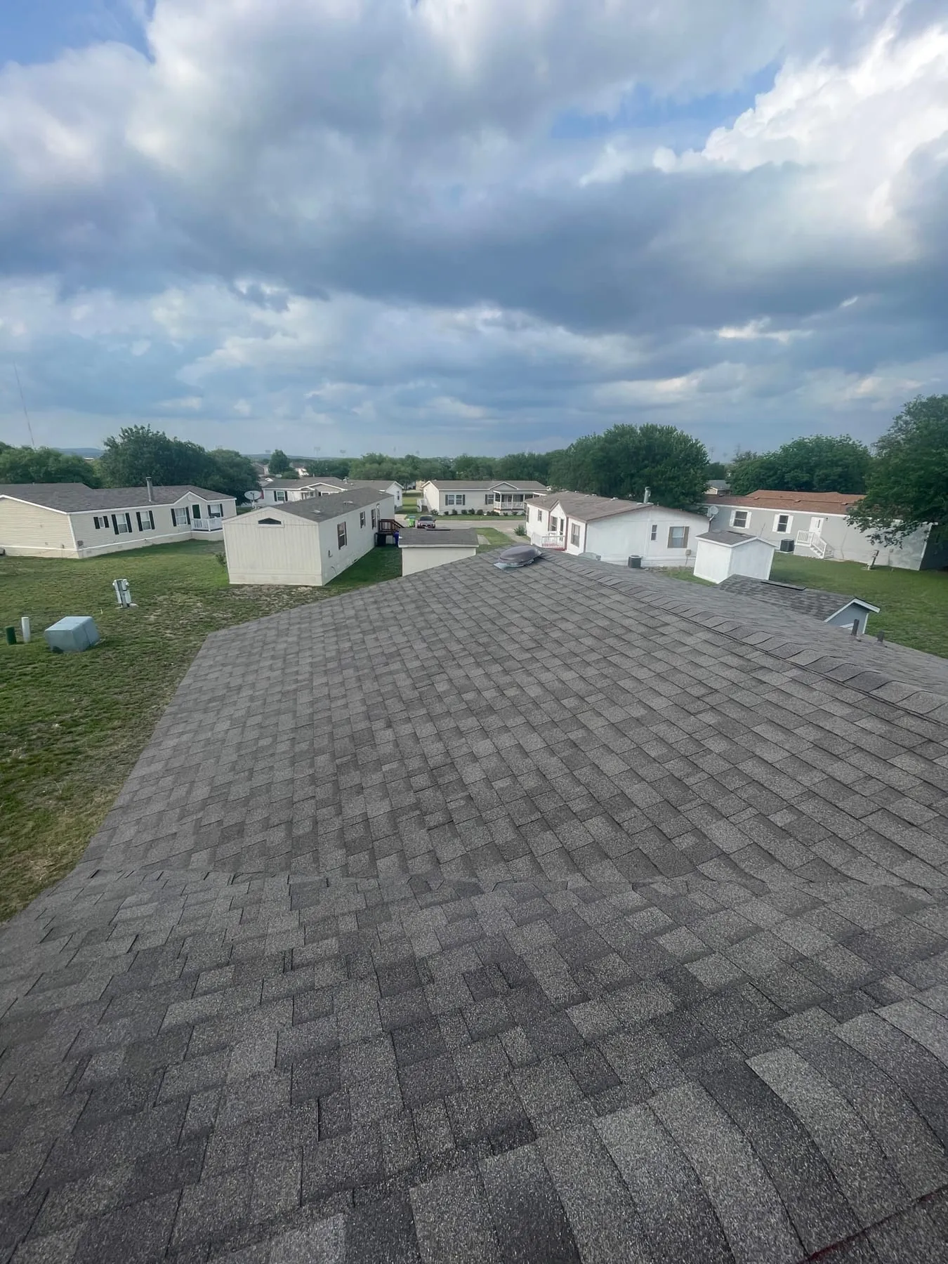 A freshly installed gray shingle roof seen from the ridge, looking out over a residential community near San Antonio, Texas